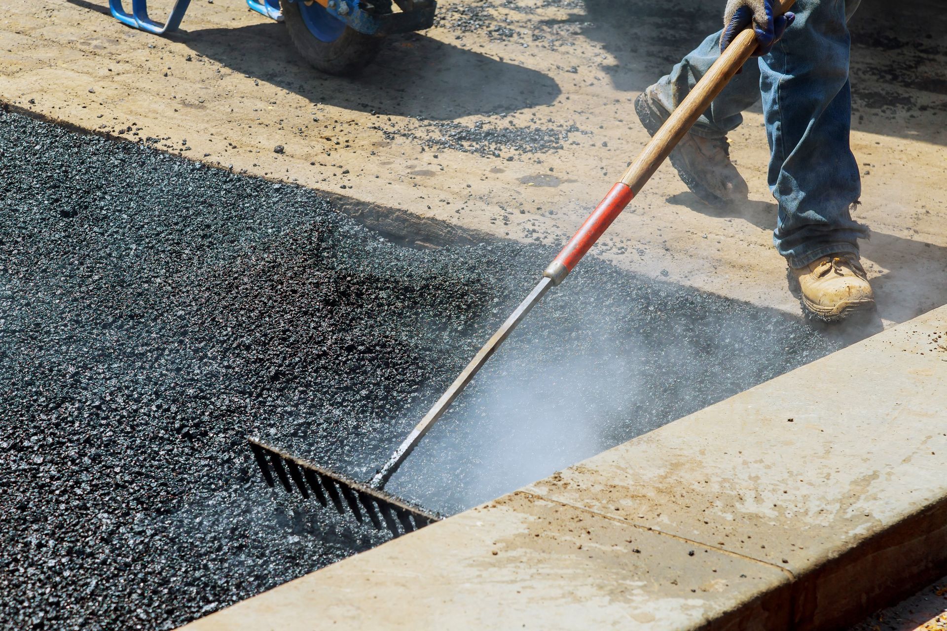 Man rakes steaming asphalt on a concrete surface.