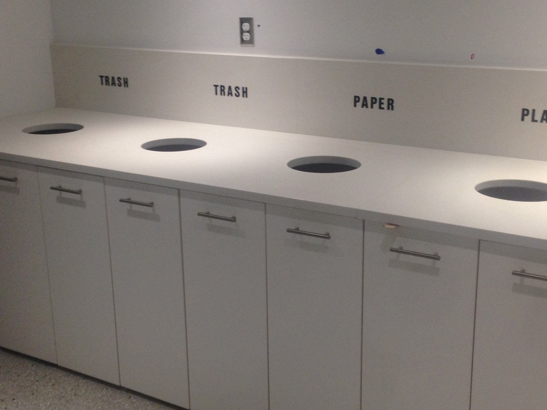 A row of white cabinets with trash paper and plastic bins