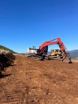 Red excavator and yellow bulldozer on a cleared dirt path under a blue sky.