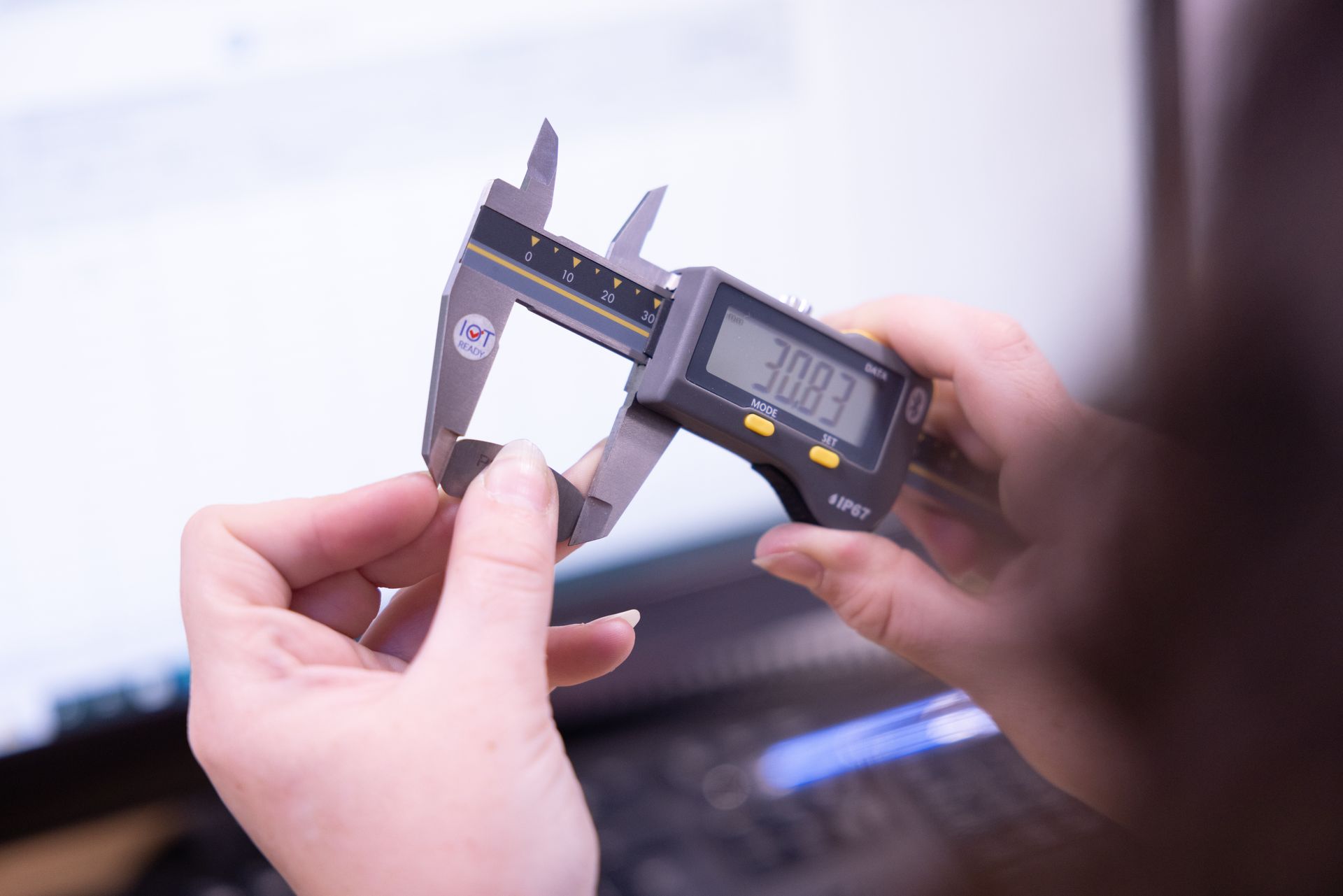 A person is measuring a piece of metal with a digital caliper.