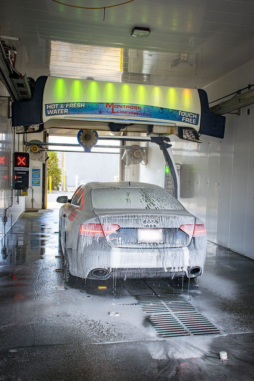 Car being washed at a car wash, covered in soap, inside an automated structure.