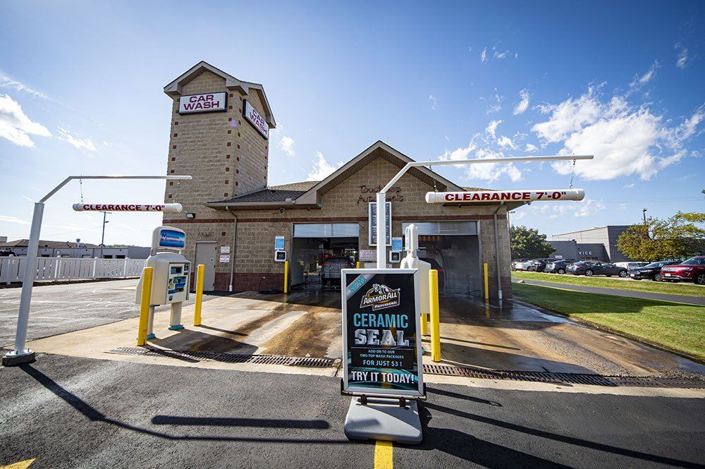 A car wash with a tall brick tower. An advertising sign stands in the driveway. Blue sky.