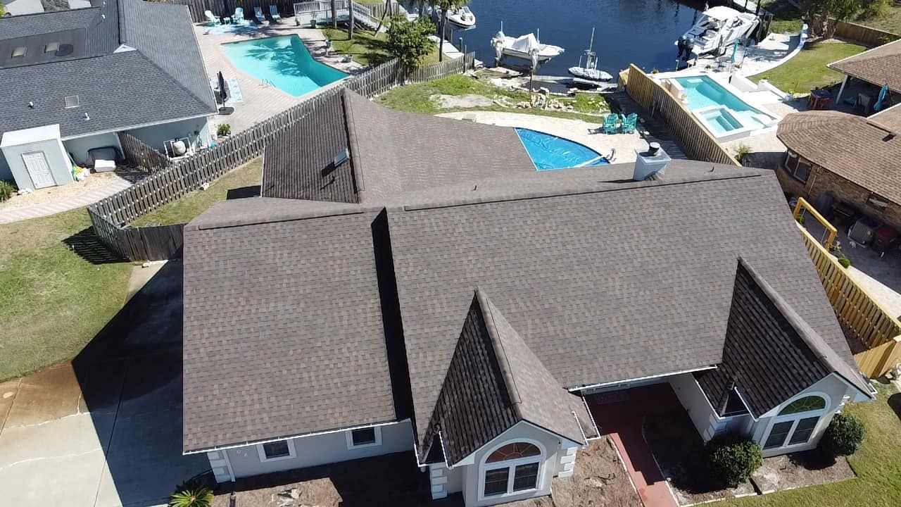 Aerial view of a brown-roofed house beside a backyard pool and patio area.
