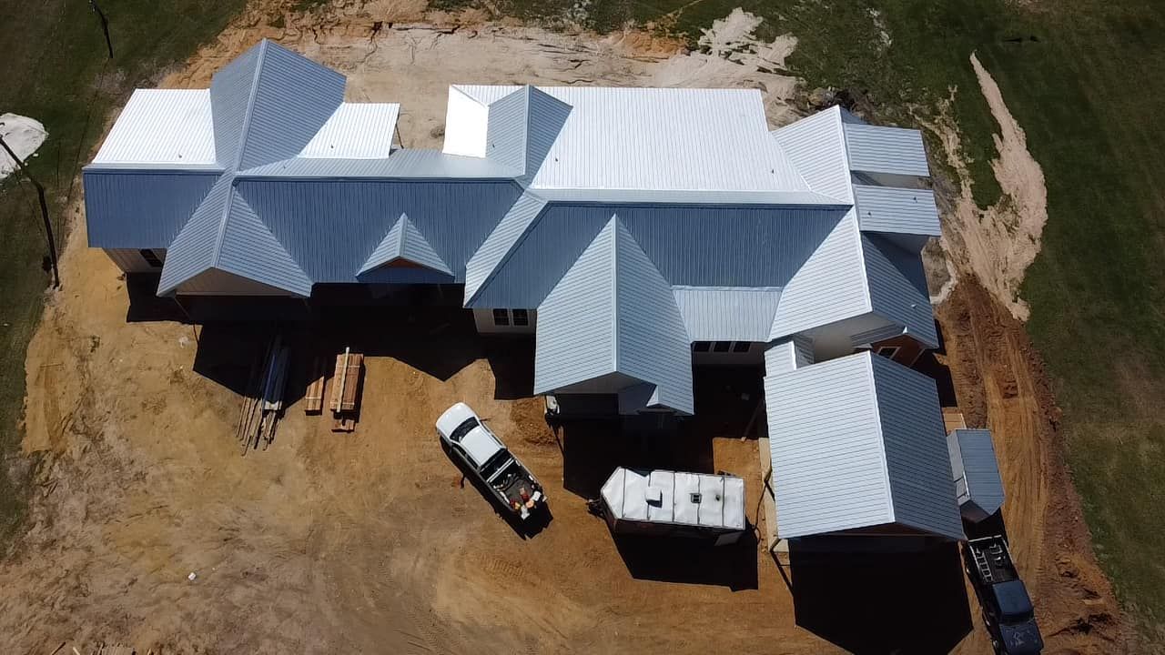 Aerial view of a large white-roofed building complex with parked vehicles on dusty ground.
