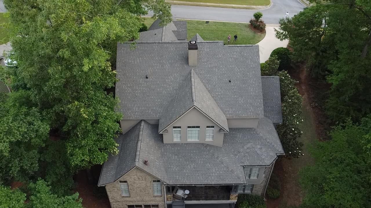 Aerial view of a gray-roofed house surrounded by trees and a driveway