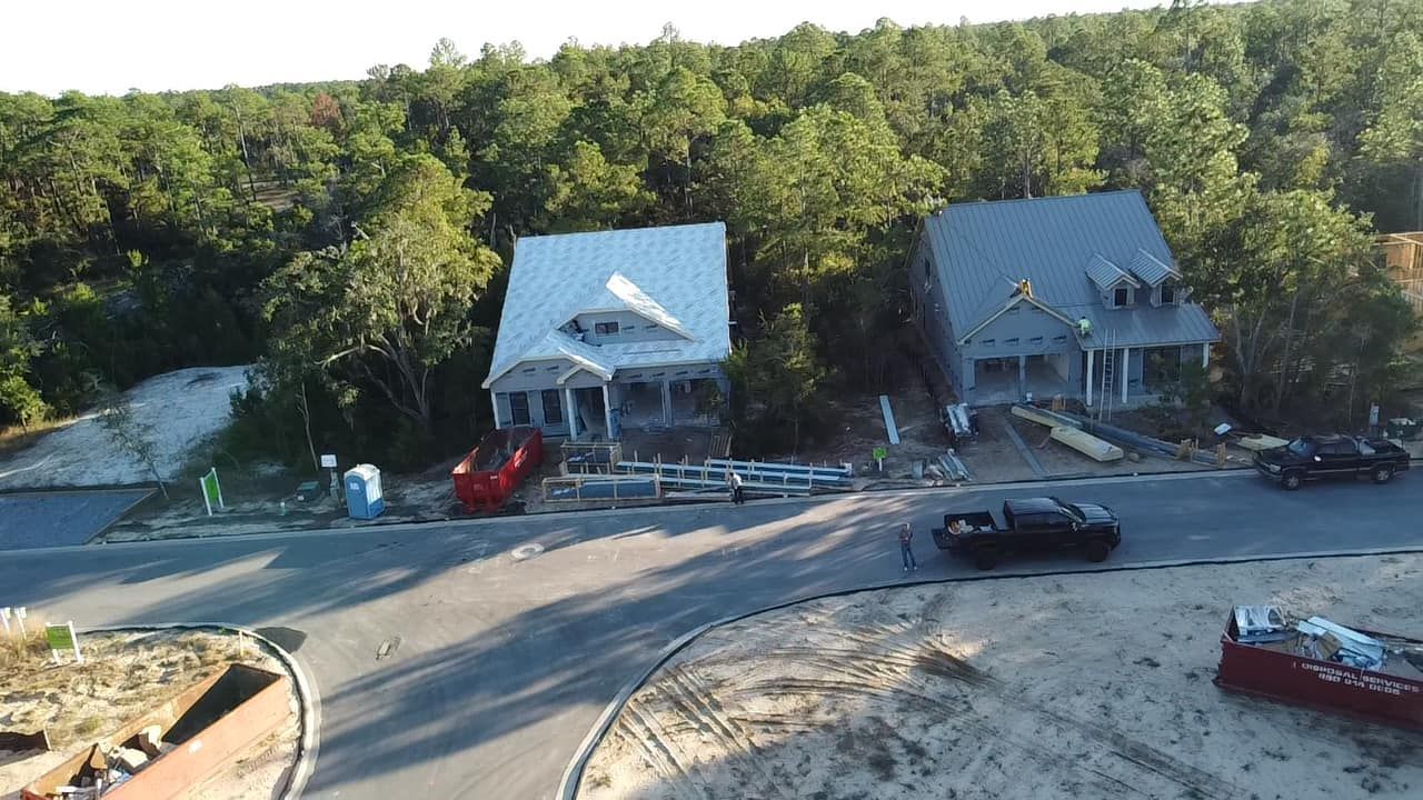 Worker in red hard hat crouching on a tiled roof, repairing shingles under a cloudy sky