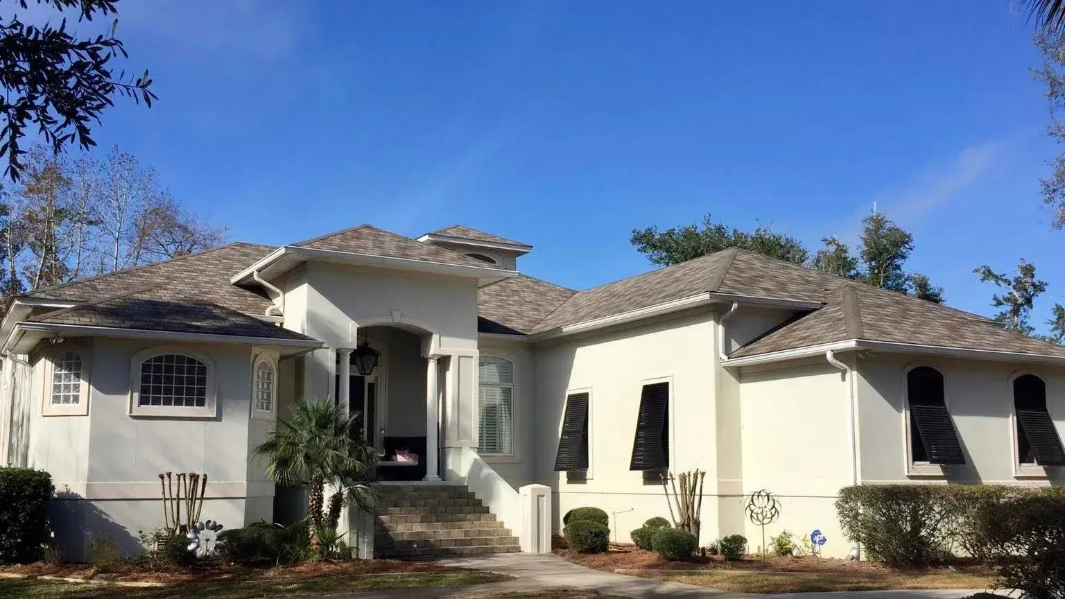 Single-story cream house with a tiled roof, arched entry, and black shutters under a clear blue sky