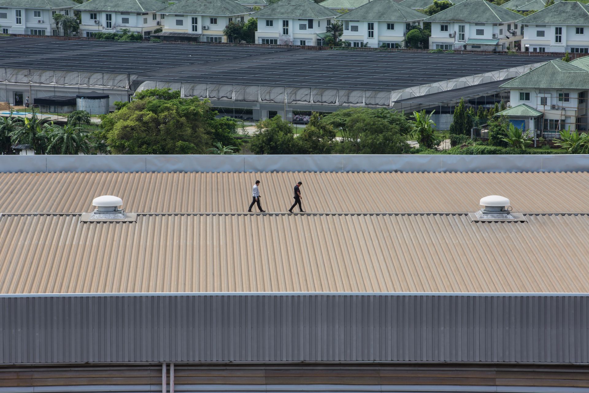 Two workers in safety gear inspecting a blue solar panel roof