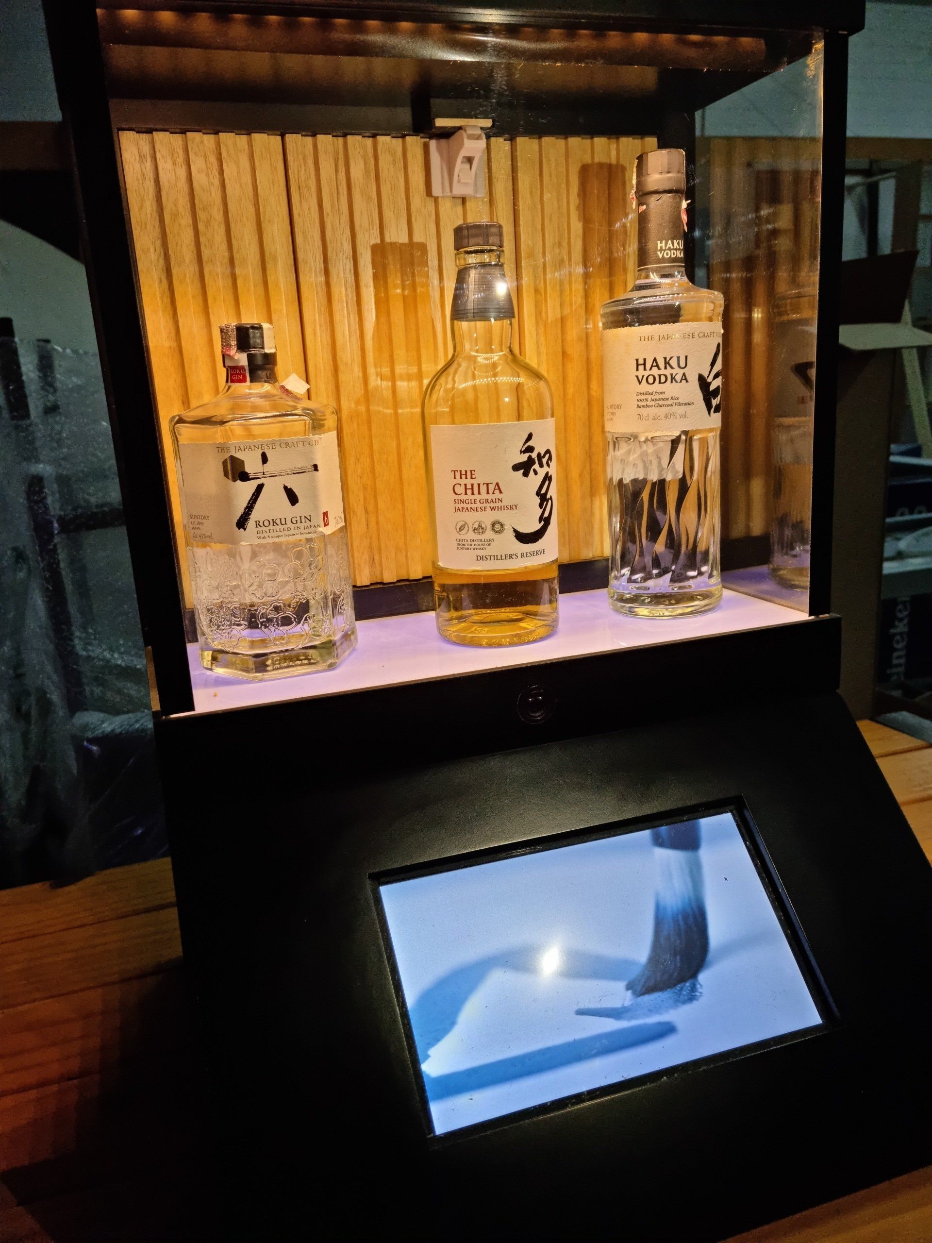 Uma vitrine com três garrafas de álcool e uma tela.