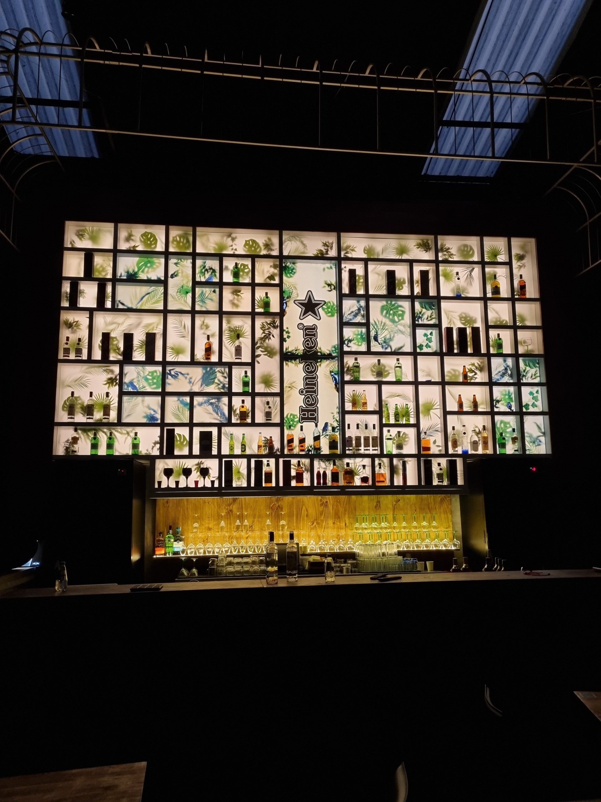 Um bar com muitas garrafas e uma tela grande atrás.