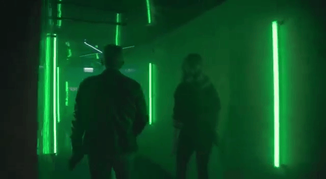Duas pessoas estão em um corredor escuro com luzes verdes.