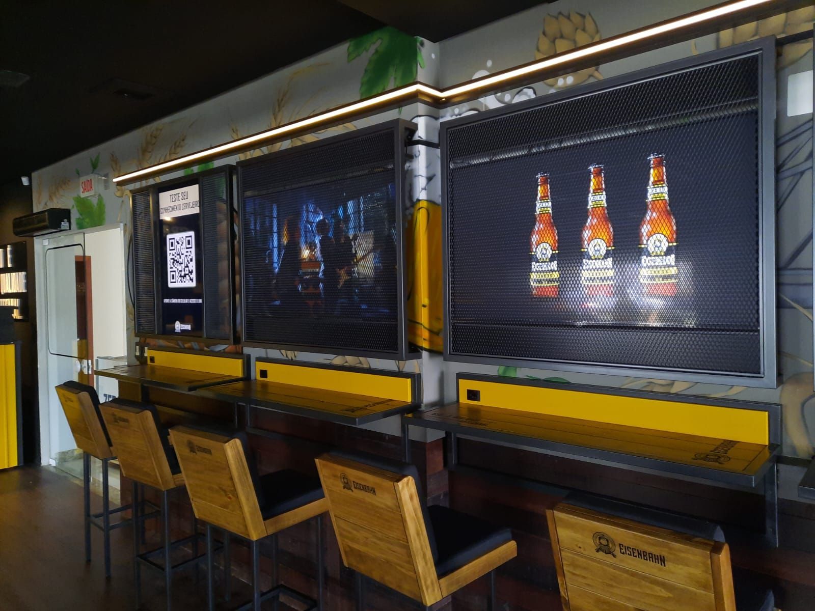 Um bar com mesas e cadeiras e uma tela grande na parede.