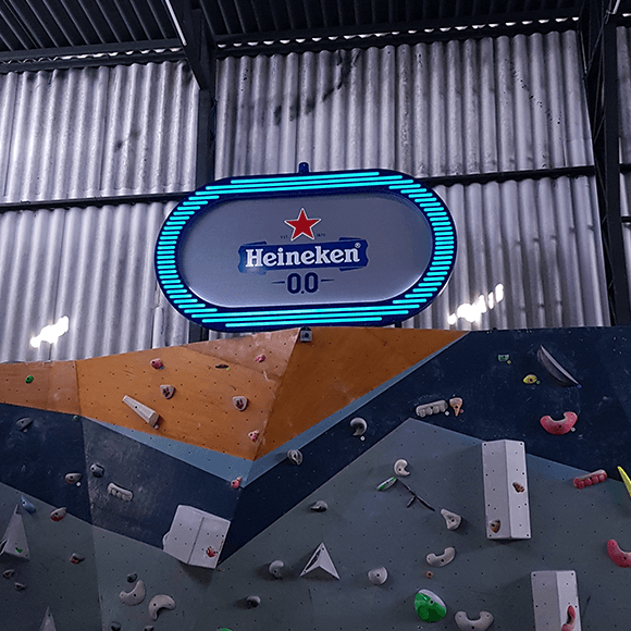 Uma parede de escalada com uma placa da Heineken acima dela