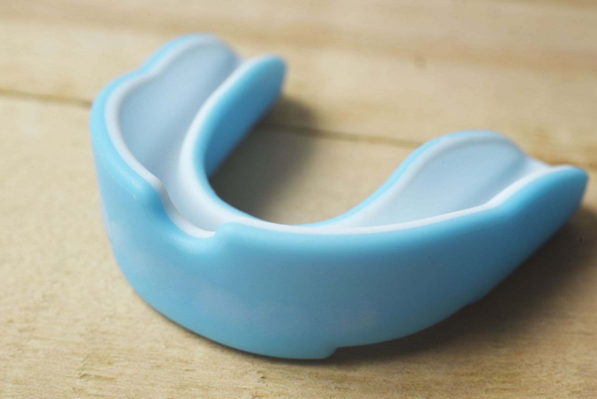 A Blue and White Mouth Guard is Sitting on a Wooden Table — The Denture Kitchen in Maroochydore, QLD