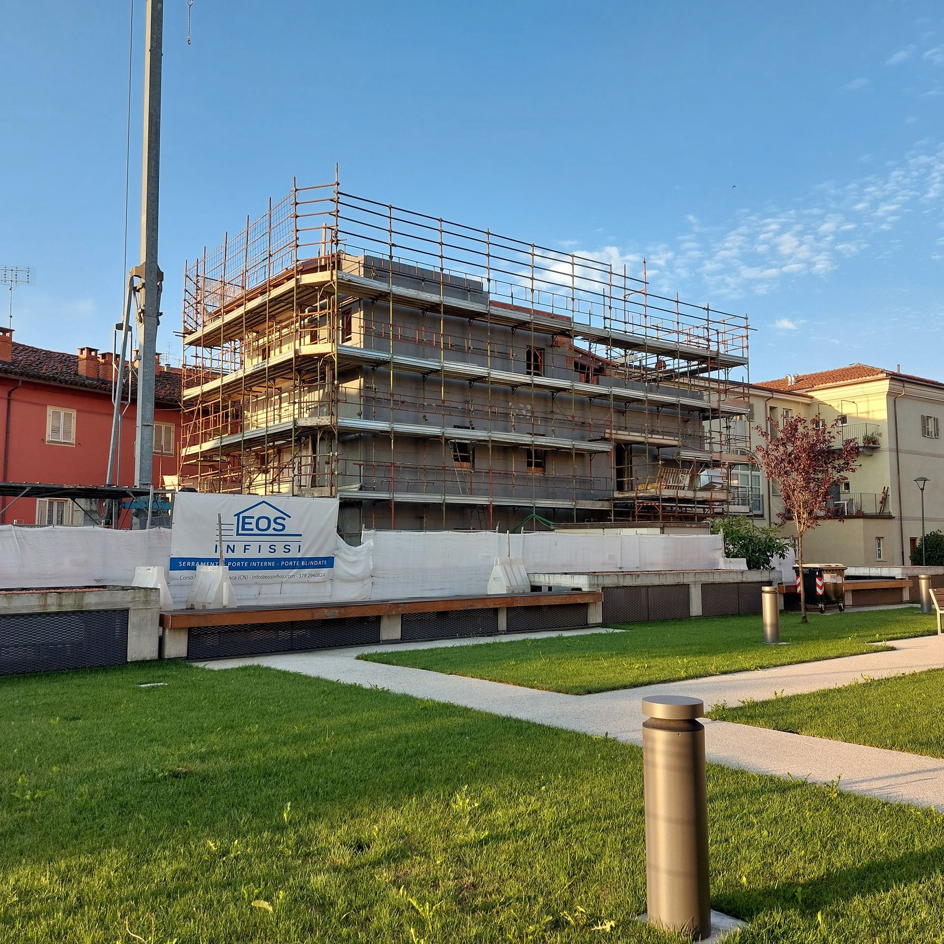 Edificio beige a due piani con balconi, persiane grigie, ringhiere in vetro e un prato verde.
