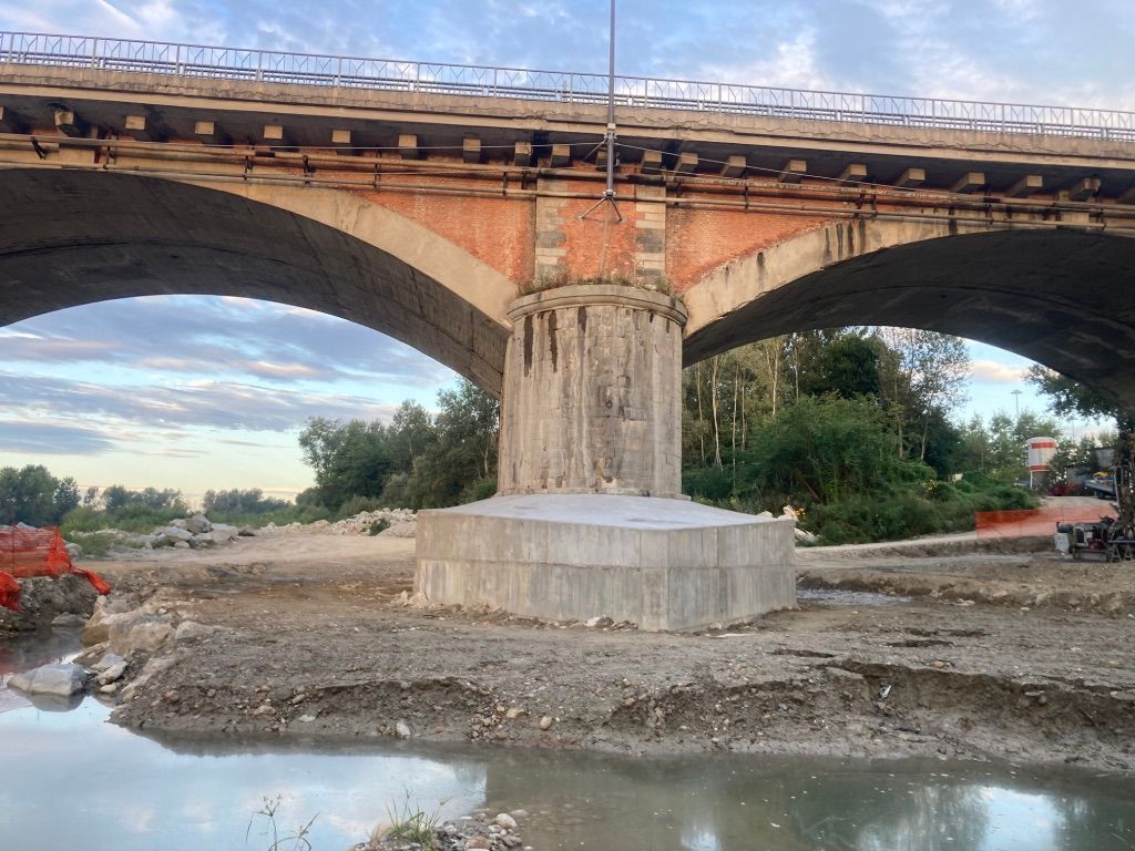 Supporto in cemento per ponte in una zona rocciosa e asciutta, illuminata dalla luce solare.
