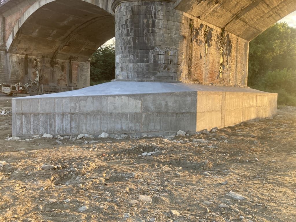 Supporto in cemento per ponte in una zona rocciosa e asciutta, illuminata dalla luce solare.