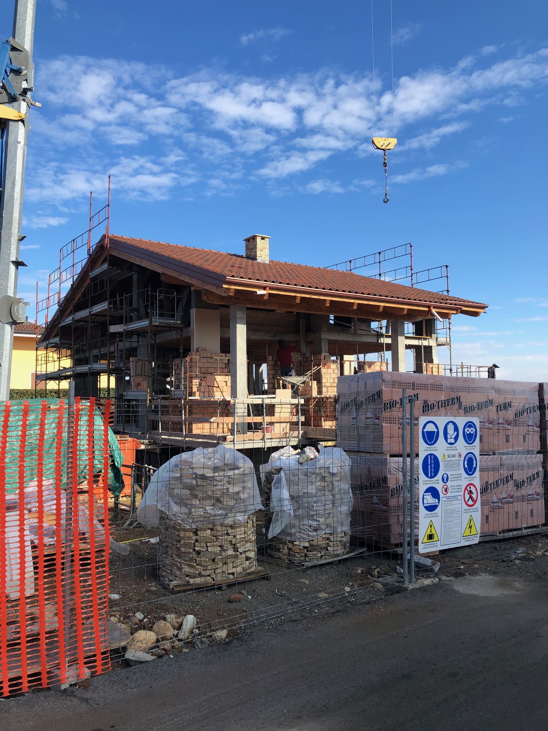 Cantiere: edificio con mattoni a vista, impalcature e pile di mattoni, cielo azzurro.