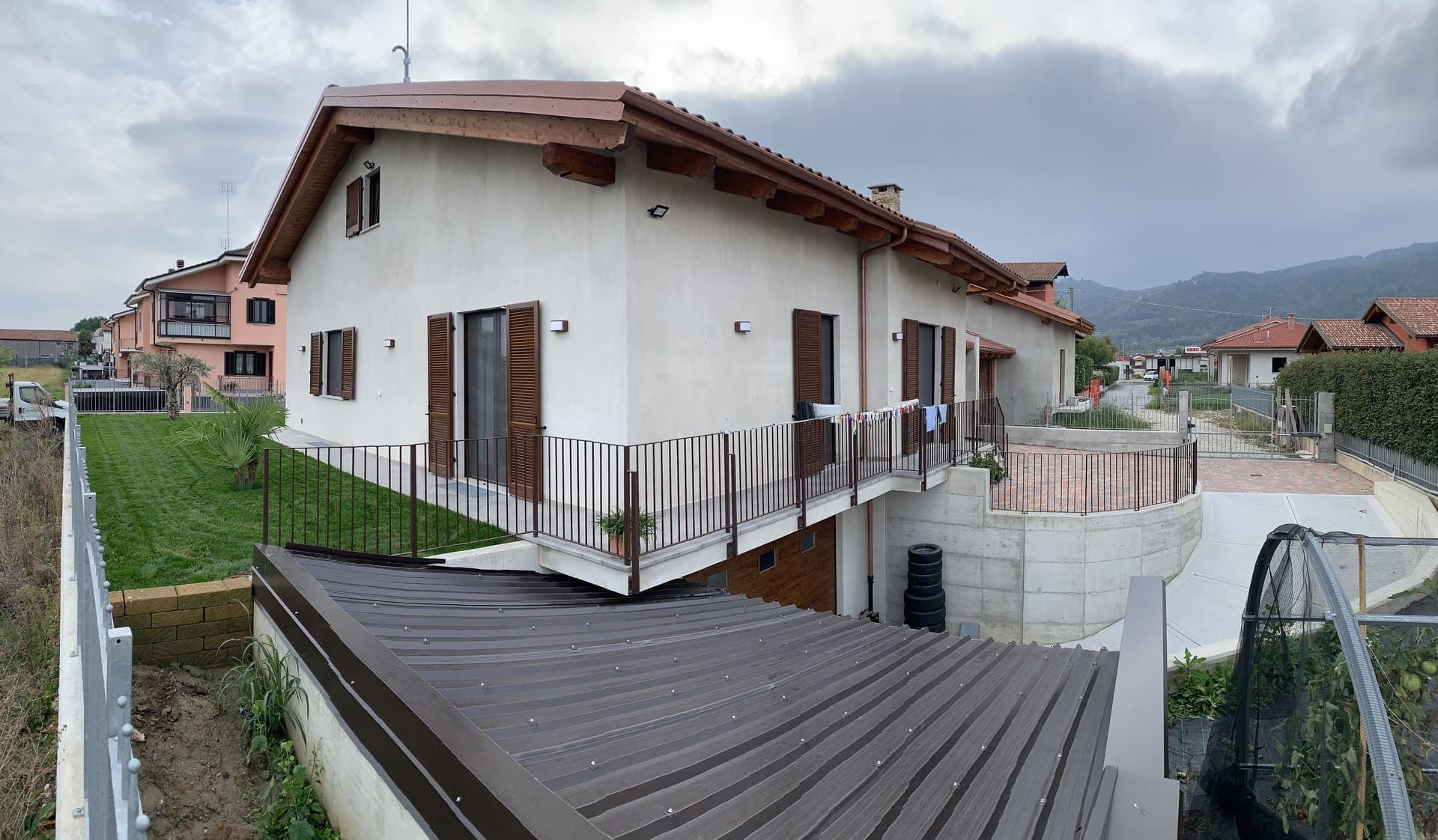 Casa bianca con persiane marroni e balcone; cielo nuvoloso.