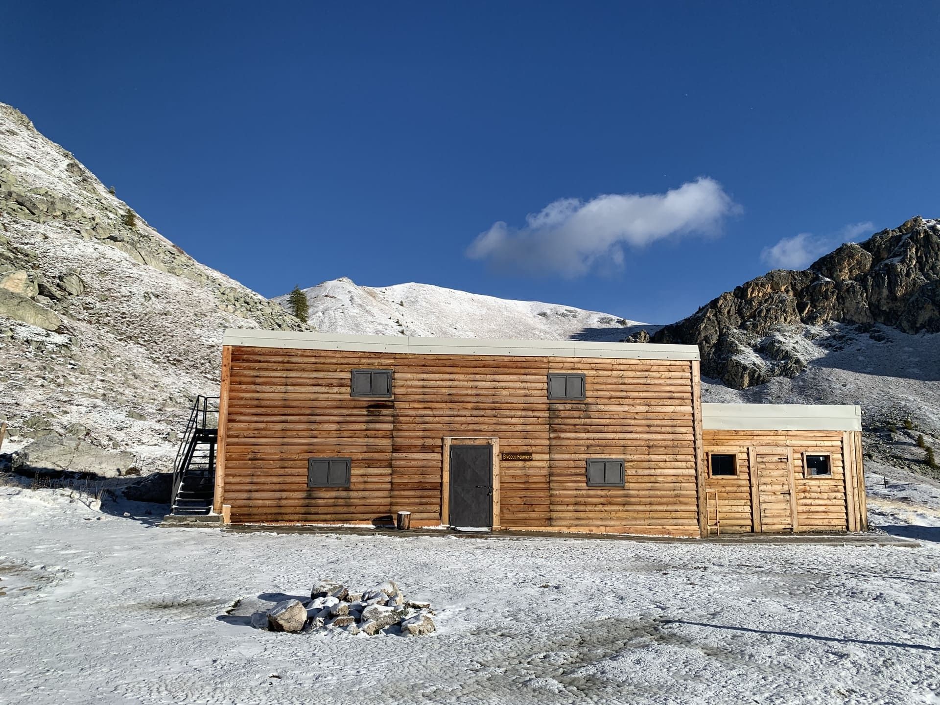 Baita di legno in un paesaggio montano innevato sotto un cielo azzurro.