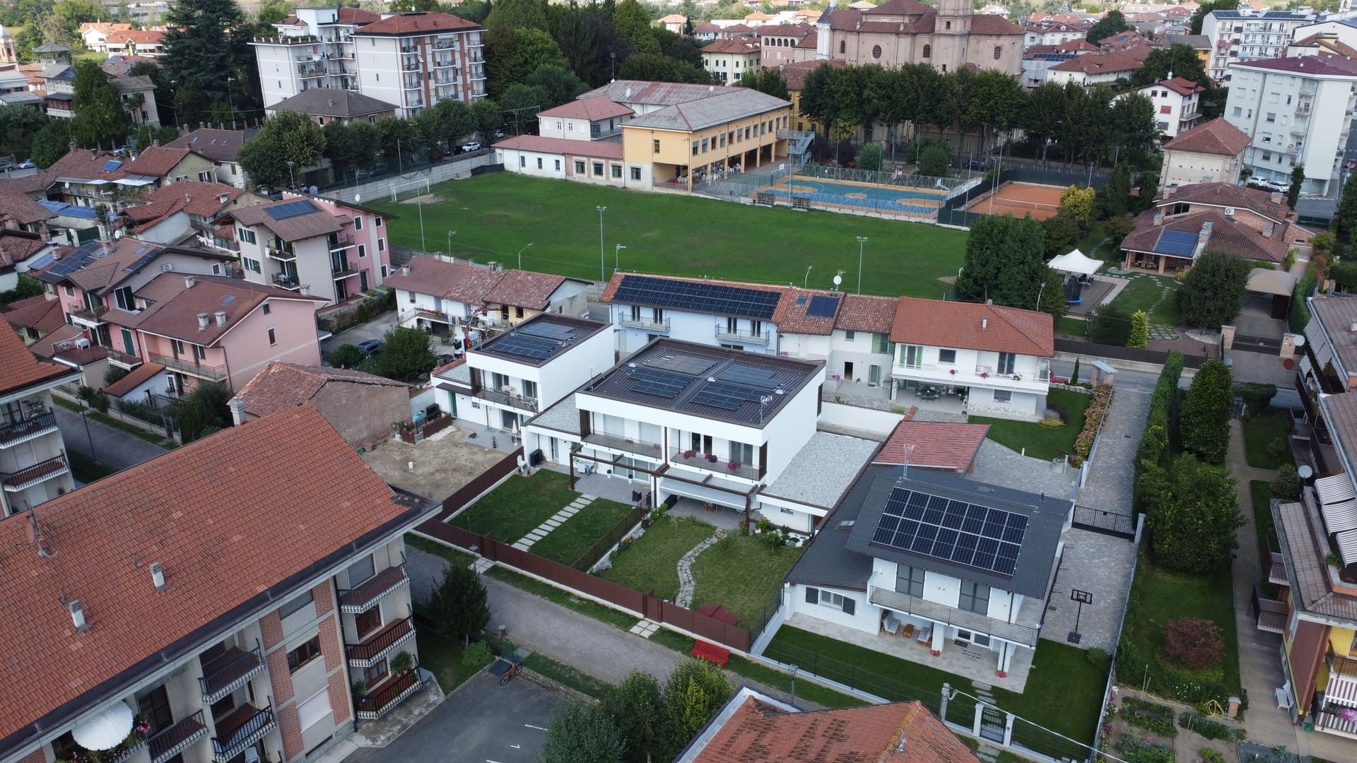 Callimaco - Centallo. Vista aerea di una città con edifici residenziali, un campo sportivo e pannelli solari sui tetti.