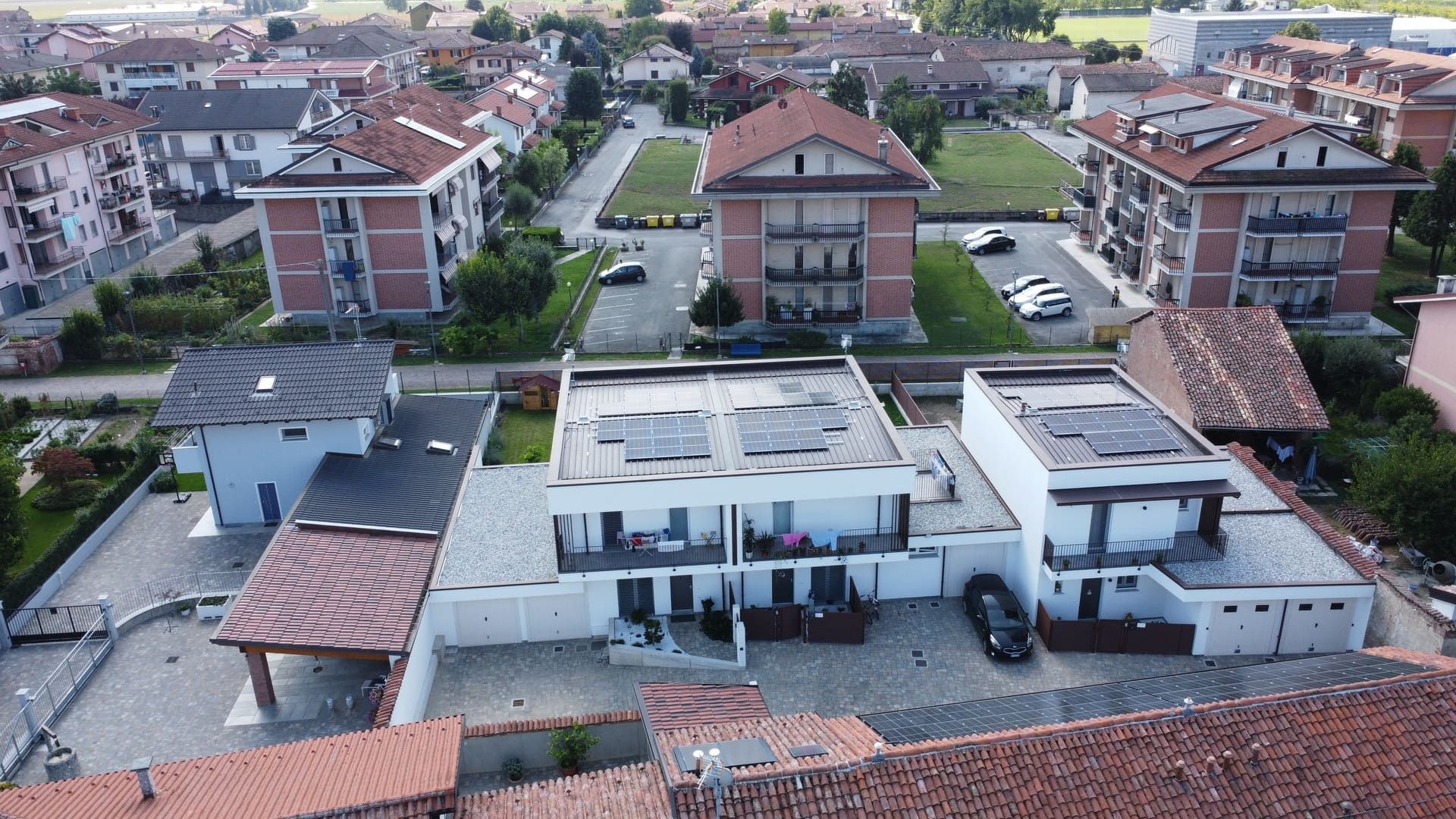 Callimaco - Centallo. Vista aerea di edifici residenziali con tetti piani e in tegole rosse, automobili e vegetazione.