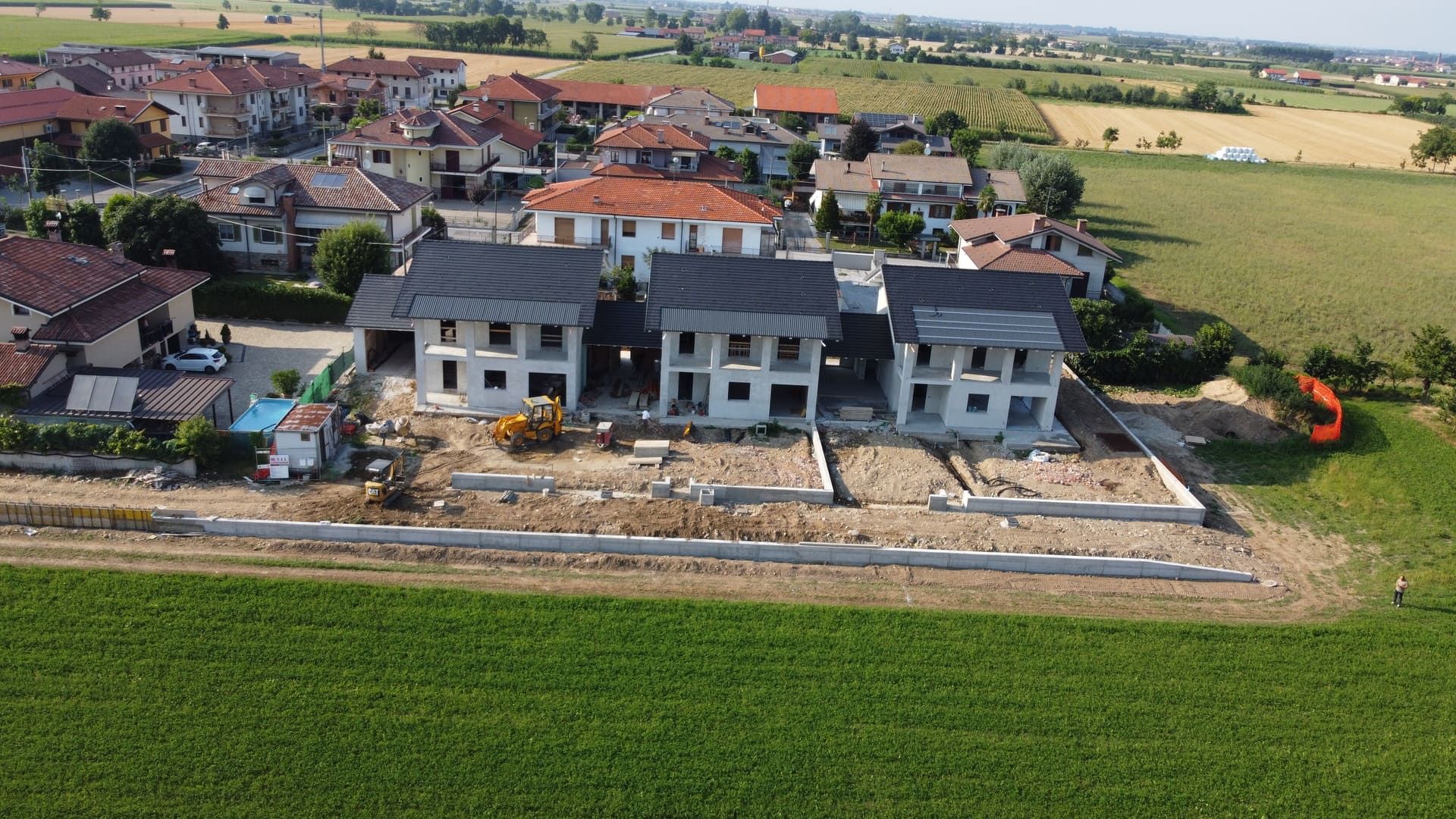 Cassandra - Roata Chiusani. Costruzione di case in un ambiente rurale, con esterni in cemento grezzo e campi verdi circostanti.