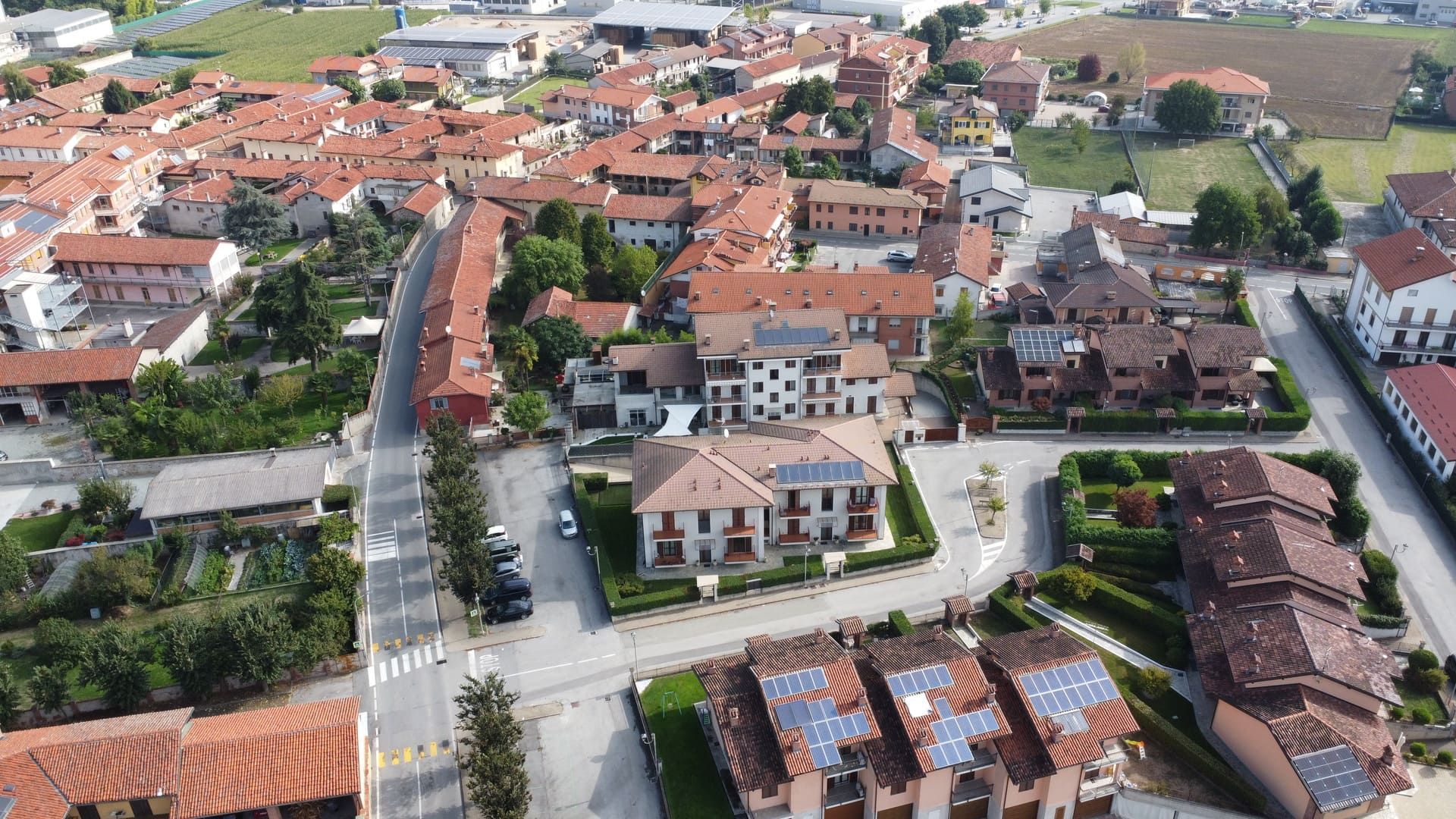 Isotta - Villafalletto. Vista aerea di una città  con tetti di tegole rosse, alberi verdi e strade asfaltate.