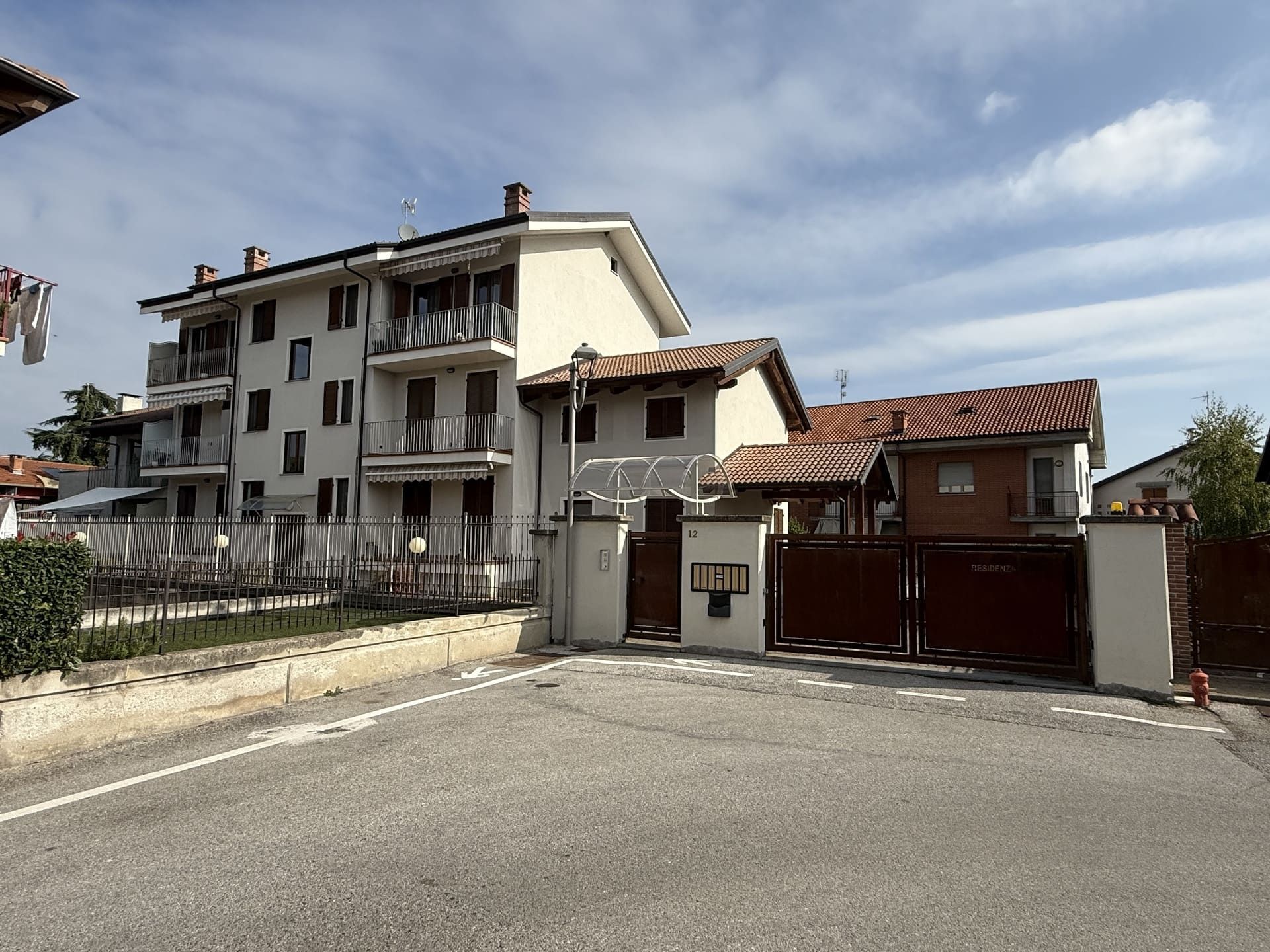 Isotta - Villafalletto. Condomini con balconi e cancelli marroni sotto un cielo nuvoloso.