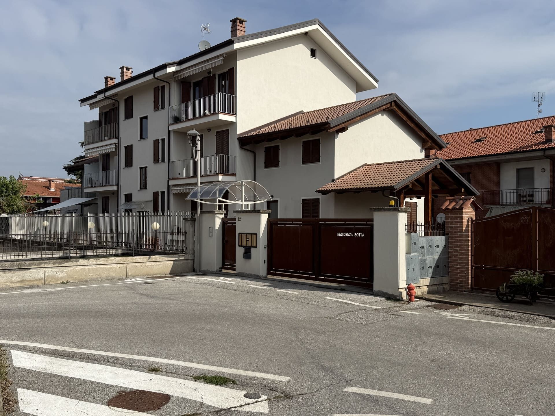 Isotta - Villafalletto. Edificio residenziale color crema e marrone con ingresso recintato e casa adiacente.