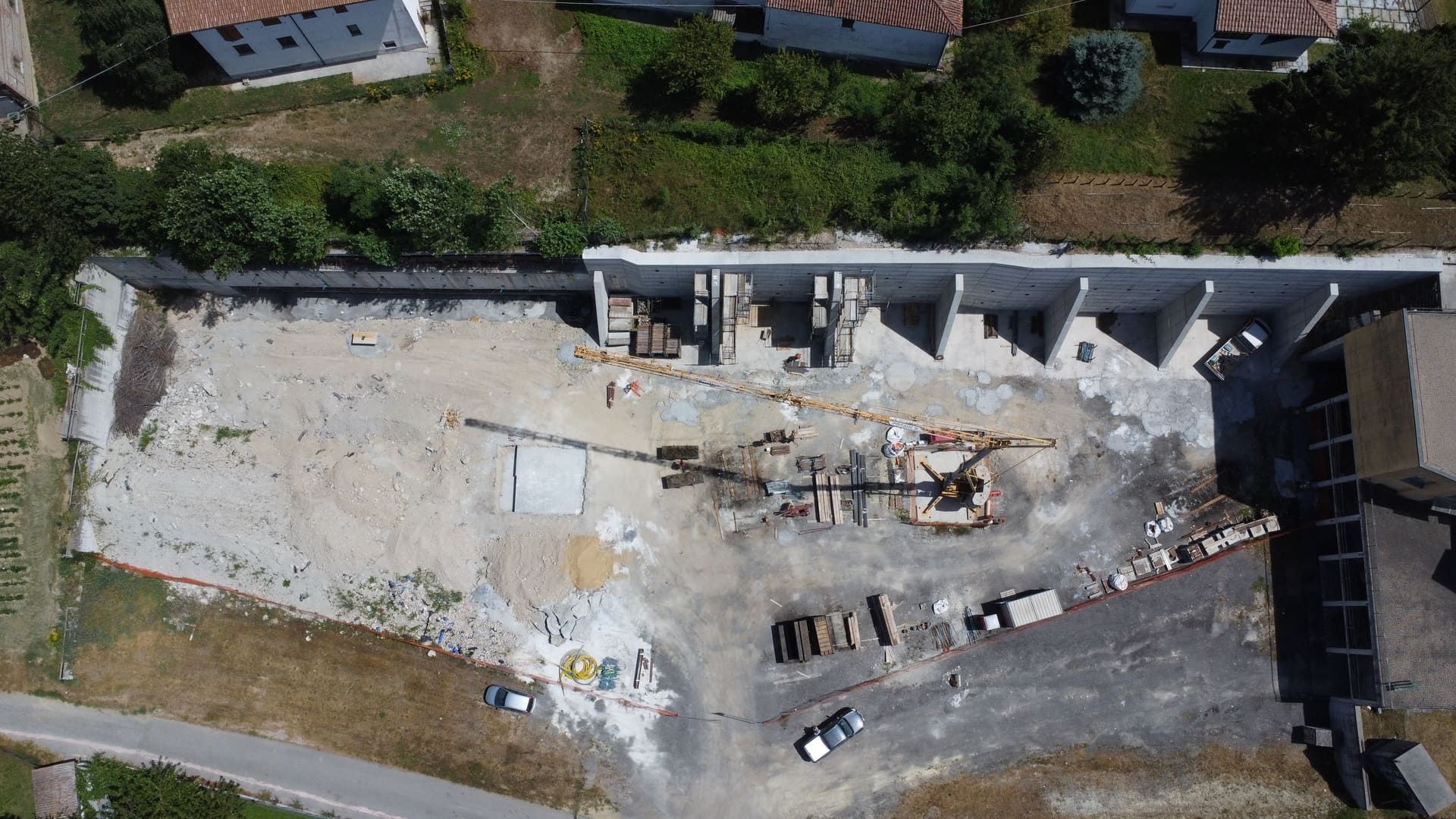 Vista aerea di un cantiere edile con macchine movimento terra, muri di cemento e materiali da costruzione.