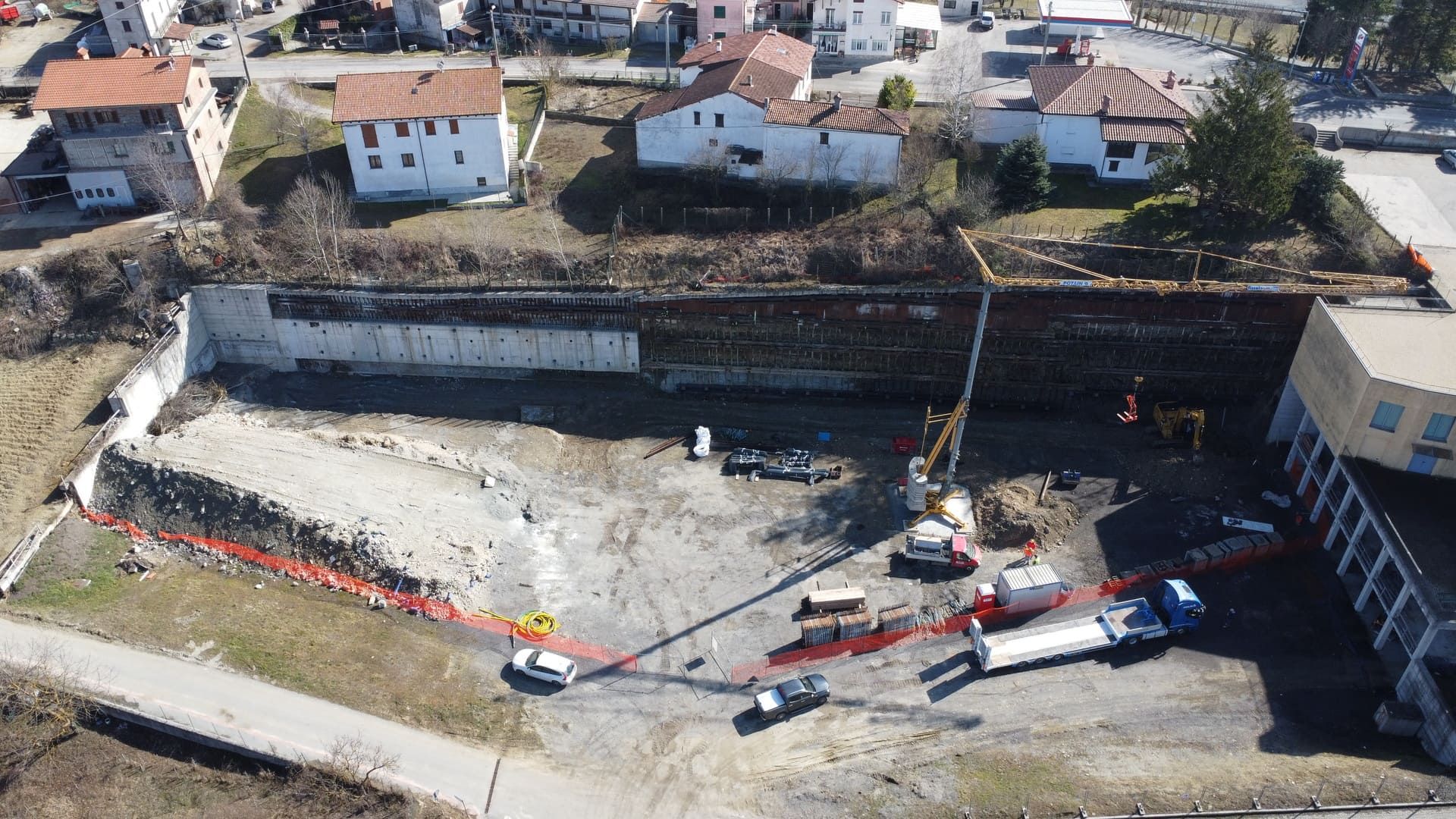 Cantiere con macchinari pesanti, muri di contenimento ed edifici.