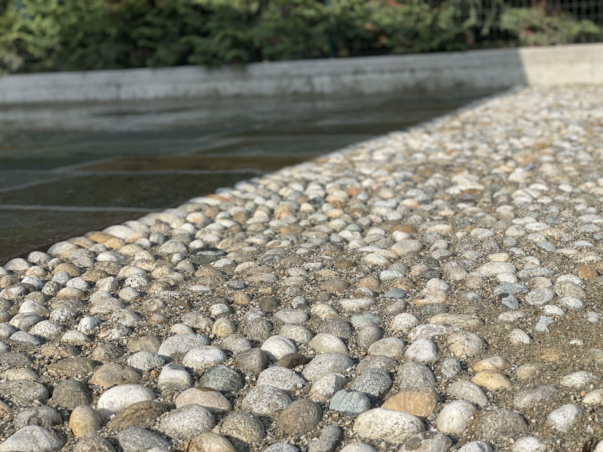 Pavimentazione in pietra con una barriera di cemento e vegetazione sfocata sullo sfondo. 