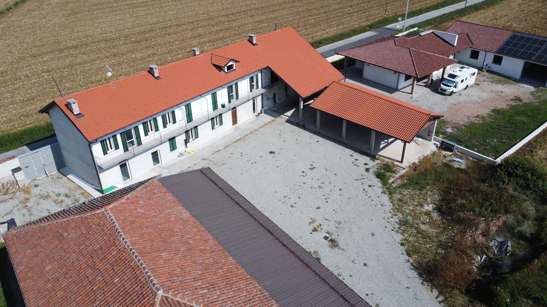 Edifici con tetti di tegole rosse in un ambiente rurale, tra cui un edificio a due piani con persiane verdi.