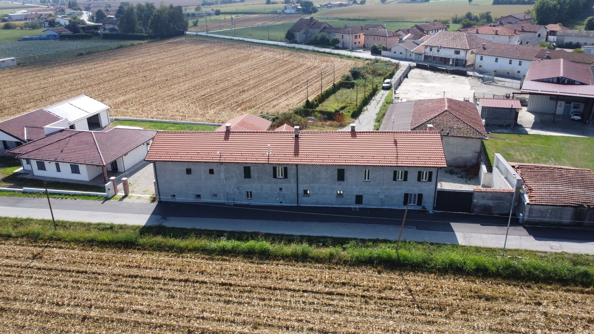 Vista aerea di un edificio in cemento con tetto in tegole rosse, campi e una piccola città sullo sfondo.