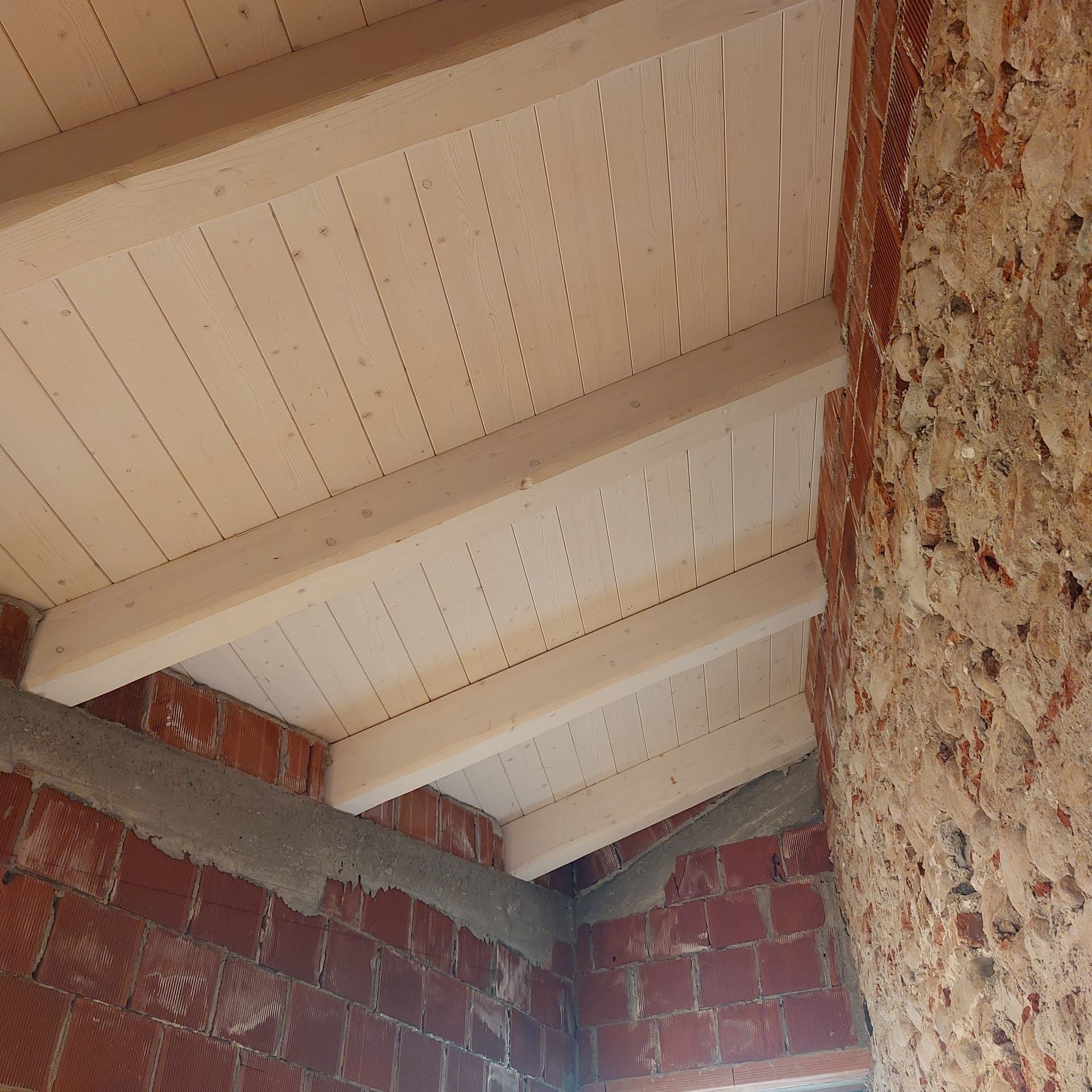 Travi e assi del soffitto in legno installate contro un muro di mattoni.