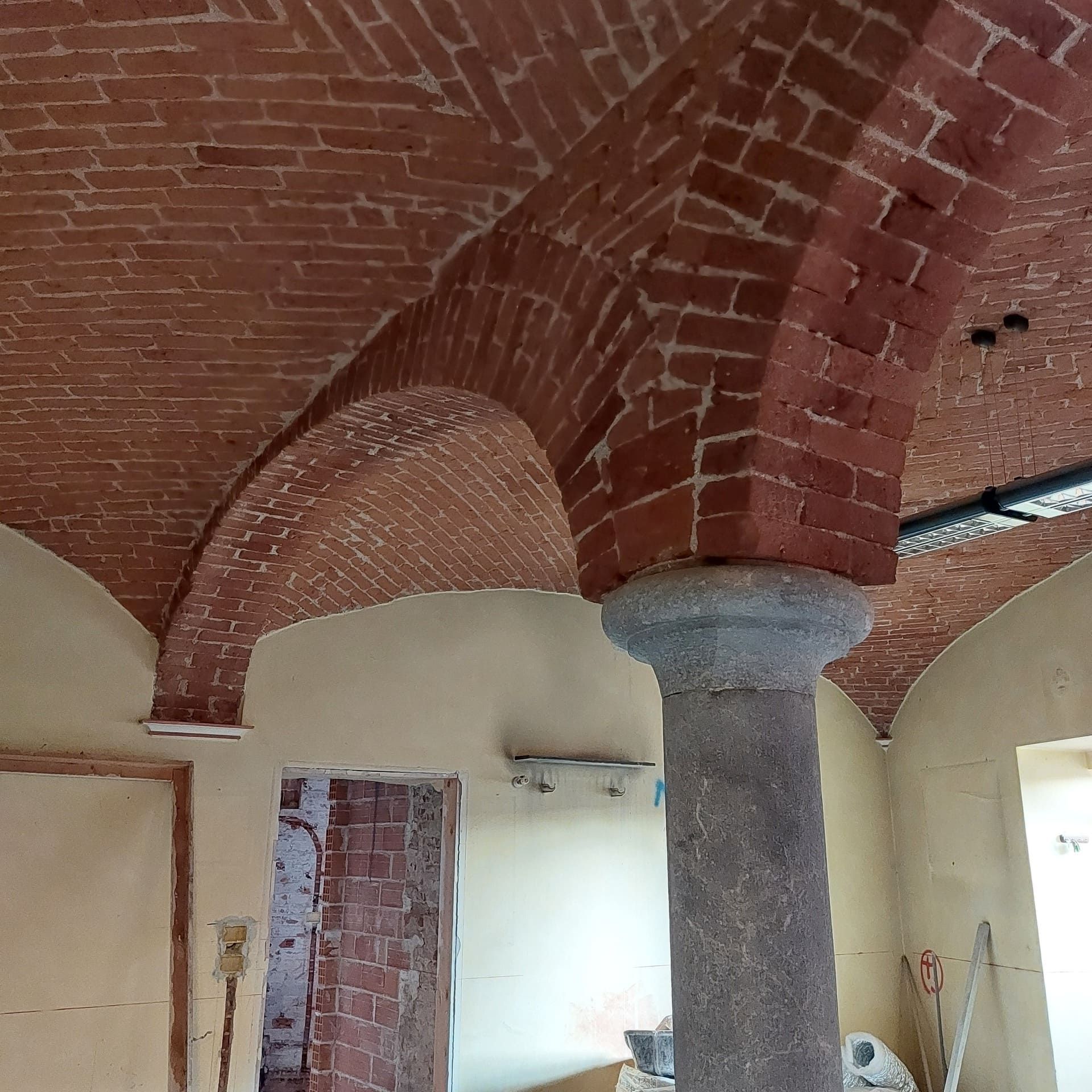 Soffitto a volta in mattoni con colonna in pietra, pareti beige e porta in costruzione.