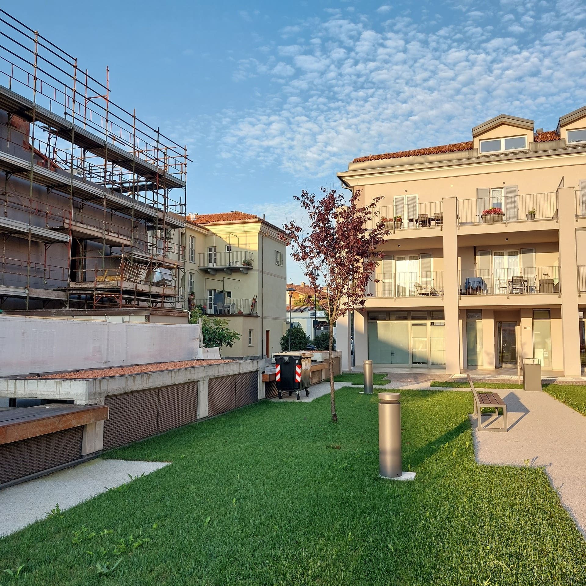 Edifici residenziali con prato erboso e un edificio in costruzione. Giornata di sole.