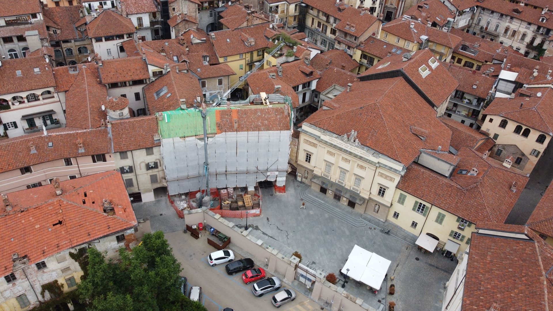 Ristrutturazione a Savigliano. Vista aerea di una piazza con edifici, automobili e impalcature edili.