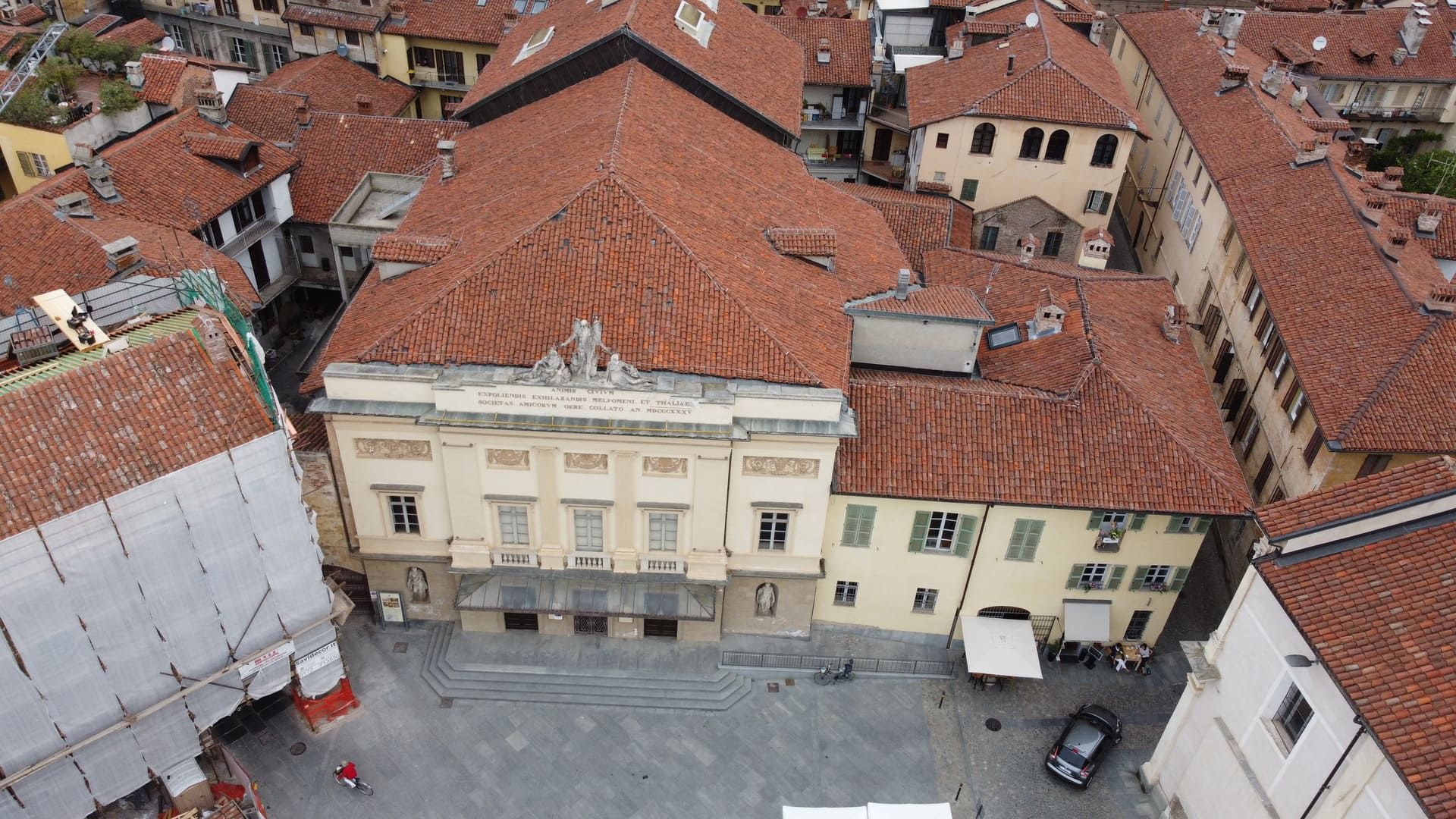 Ristrutturazione - Savigliano. Vista aerea di un edificio italiano con tetto in tegole arancioni, circondato da altri edifici e da una piazza centrale.