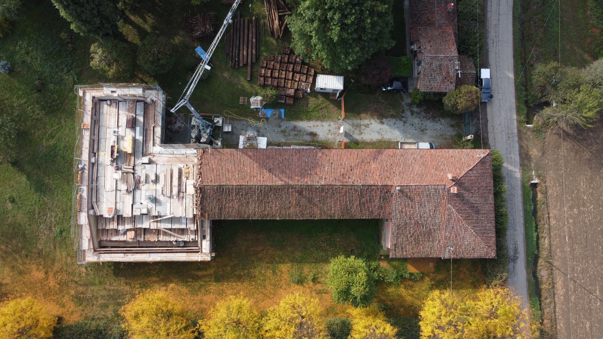 Ristrutturazione - Suniglia. Vista aerea di un edificio con tetto in tegole rosse in costruzione, con materiali da costruzione e gru nelle vicinanze.