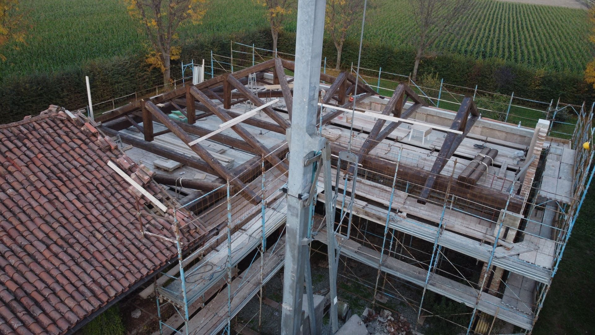 Cantiere con edificio parzialmente costruito e impalcature; tetto in tegole marroni e travi in ​​legno.