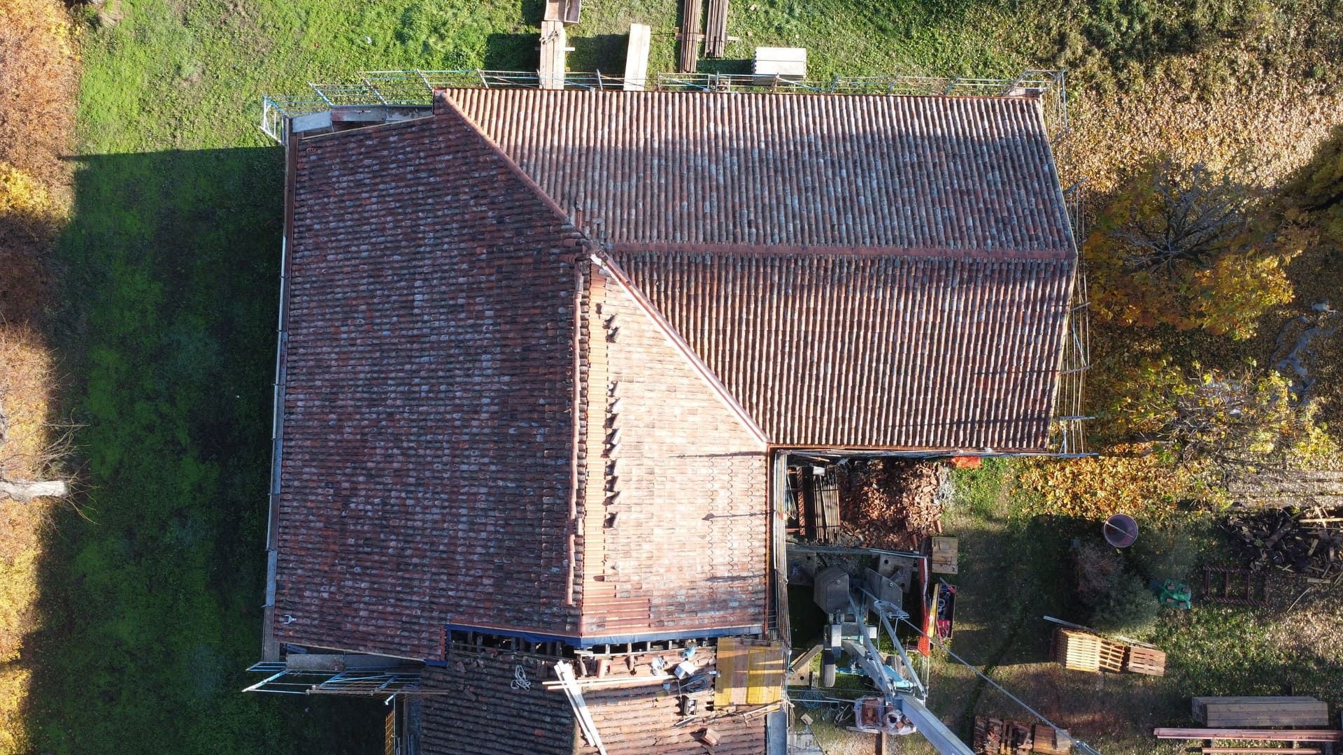 Vista aerea del tetto di una casa in costruzione, con tegole arancioni e struttura in legno a vista visibili.