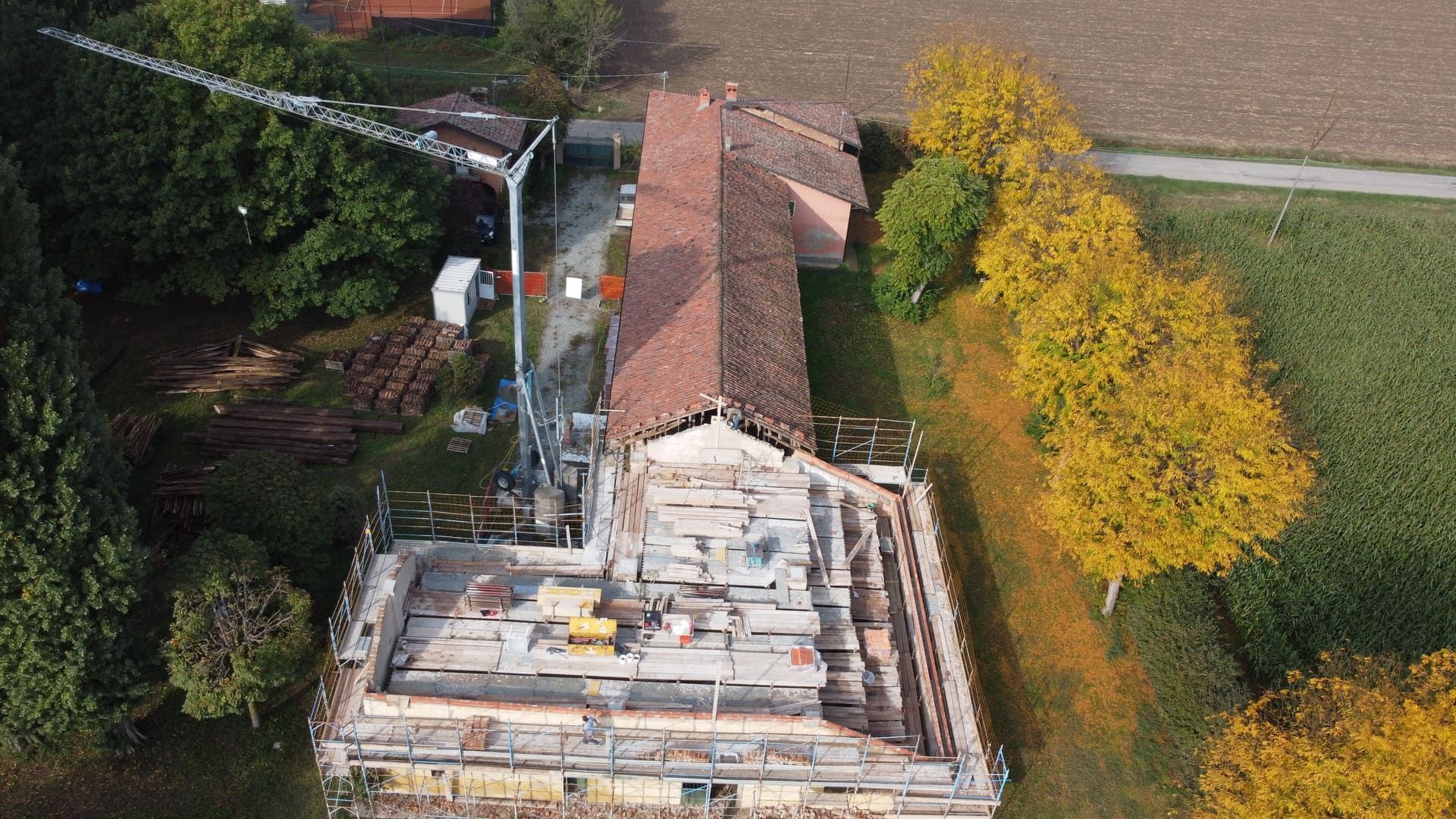 Cantiere: edificio con impalcature e gru, circondato da alberi.
