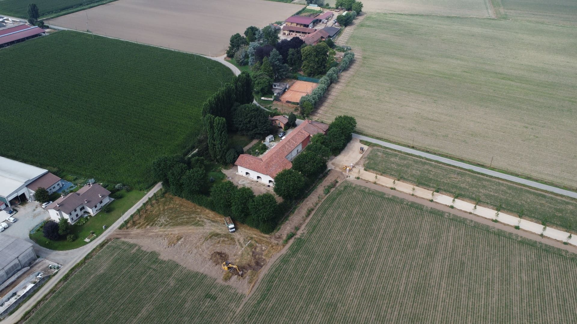 Vista aerea di una fattoria con una casa, un campo da tennis e campi circostanti di colture e alberi.