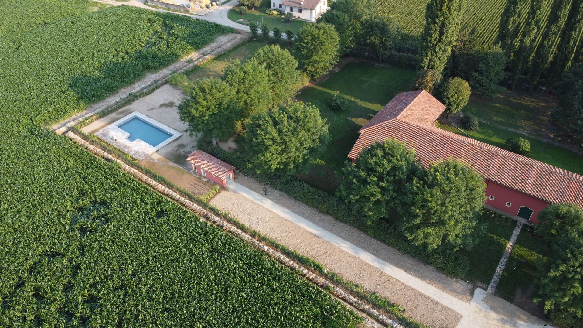 Vista aerea di un edificio con tetto rosso, piscina, vialetto d'accesso e circondato da campi verdi.