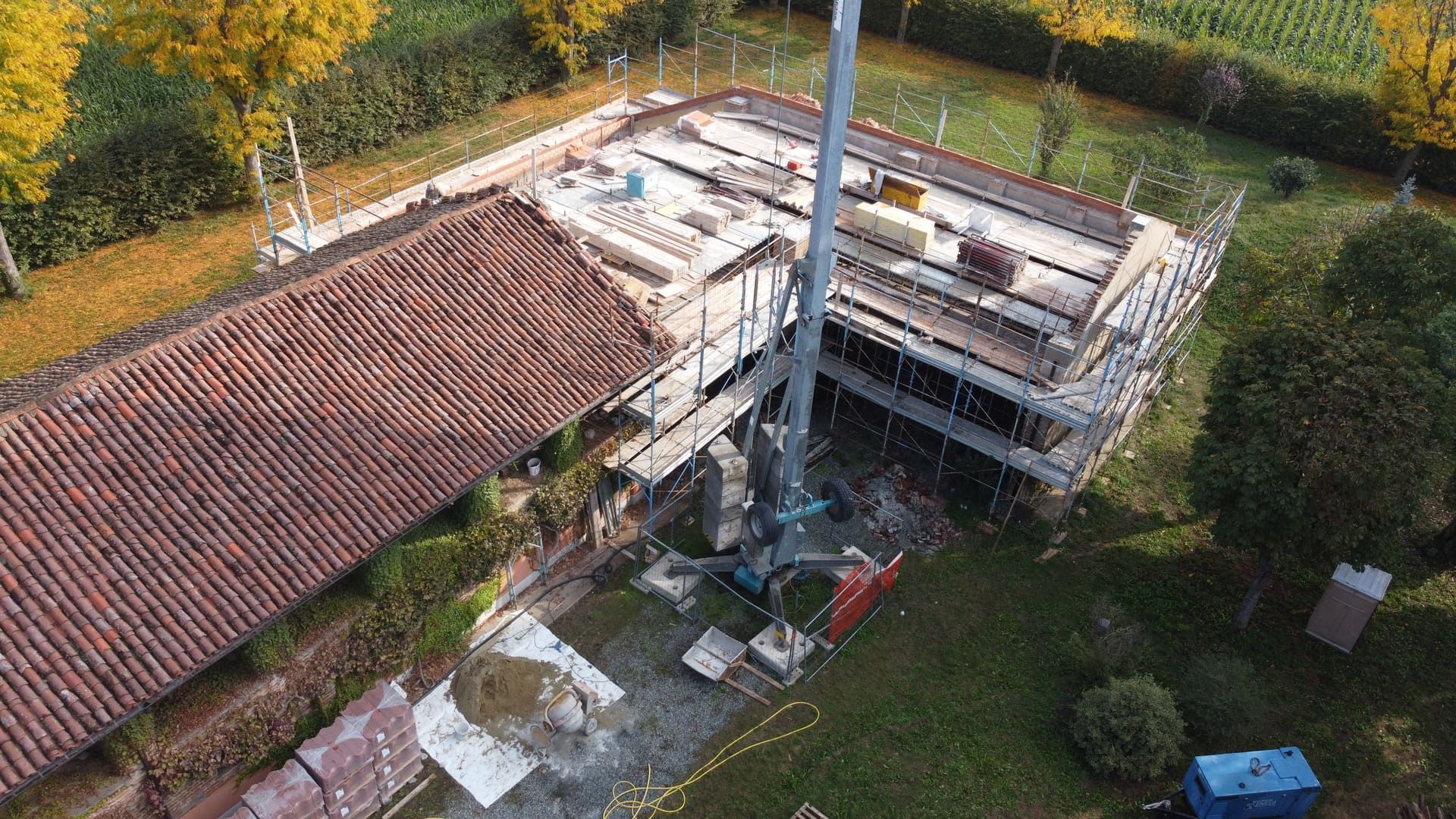 Cantiere con impalcature, gru e tetti. Erba verde e alberi.