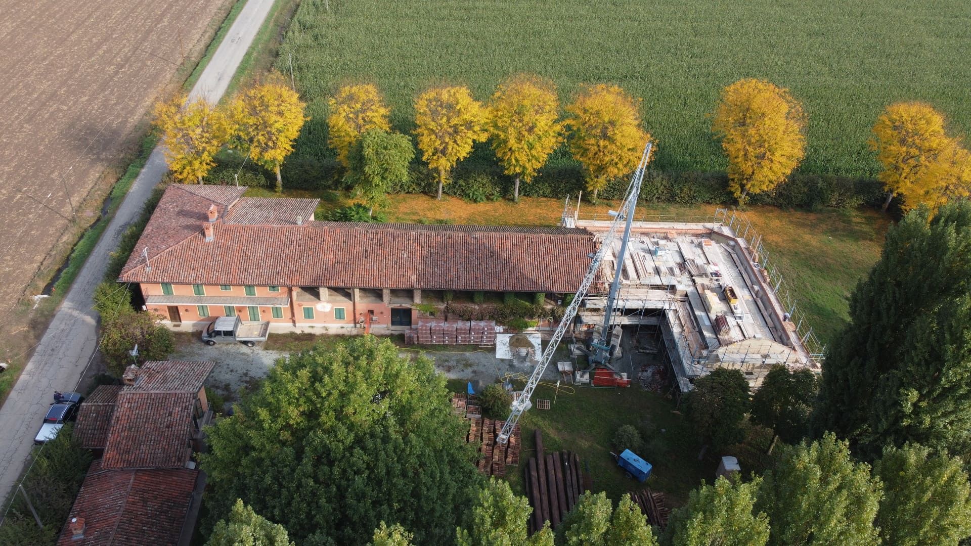 Vista aerea di un edificio in mattoni e di una nuova costruzione in un campo alberato. È presente una gru.