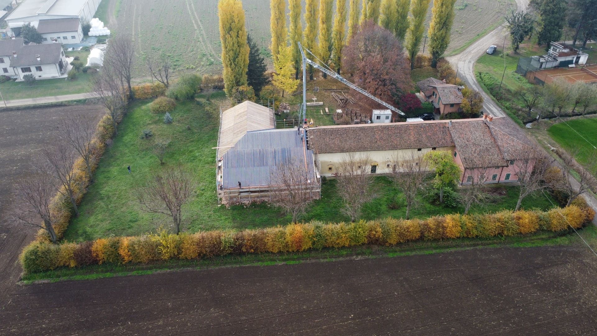 Vista aerea di un edificio rurale con un tetto rovinato dalle intemperie, circondato da campi e una siepe.