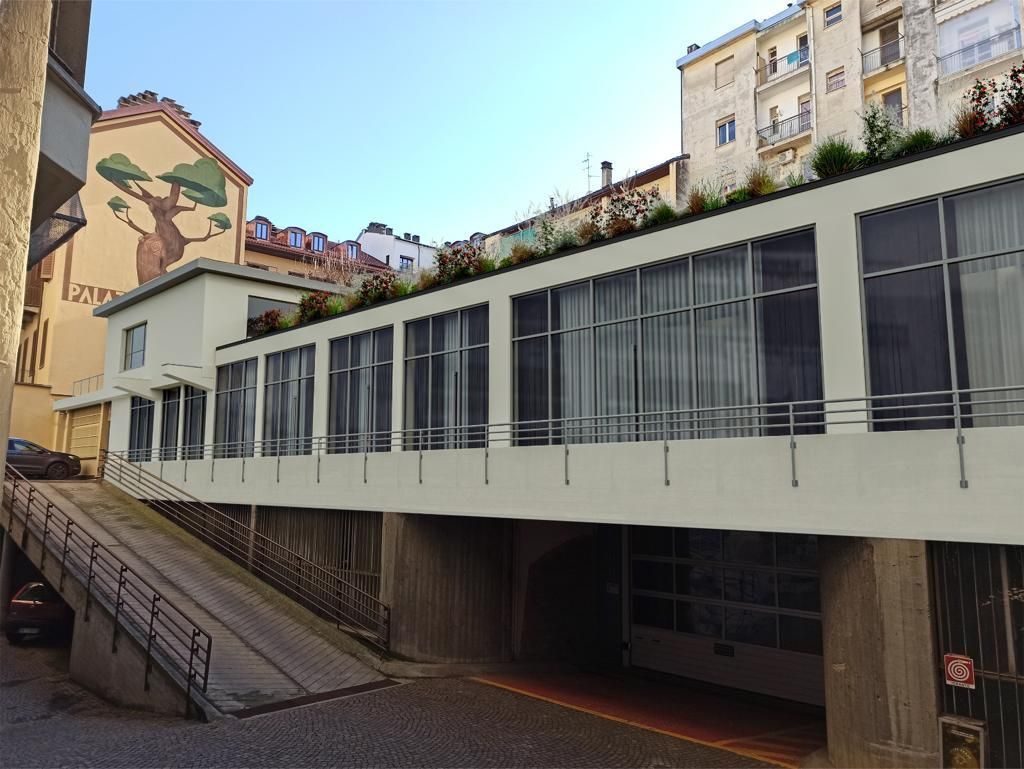 Edificio bianco con facciata in vetro, rampa sul lato sinistro e murale di un albero sulla sinistra.